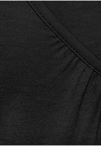 Schwarzer Stoff mit einem strukturierten Strickmuster, der entlang der Kante eine geraffte Nahtdetail aufweist und in bestimmten Bereichen eine glatte Oberfläche hat.