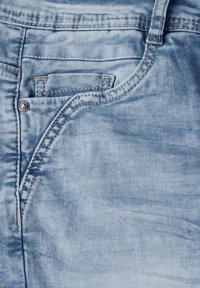 Jean en denim bleu clair avec une poche avant, des coutures contrastantes et un détail de rivet, offrant une texture lisse et une finition délavée.