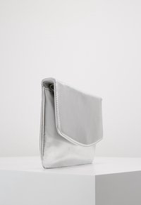 Pochette métallique argentée à la texture lisse, de forme rectangulaire, avec un rabat rabattable. Présente des détails cousus sur les bords.