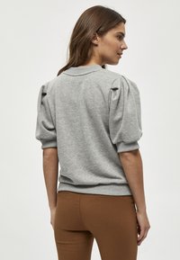 Grå sweatshirt med puffiga korta ärmar, ribbad halsringning och mudd, tillsammans med bruna figurnära byxor. Mjuk, stickad textur är synlig.