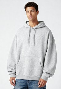 Helle graue Kapuzenjacke aus weichem Stoff, mit großer Fronttasche, Kapuze mit Kordelzug sowie gerippten Bündchen und Saum. Lässige Passform, minimalistisches Design.