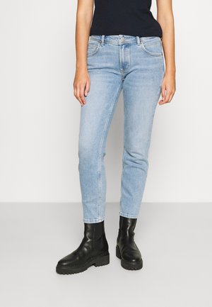 Jeans en denim bleu clair avec une coupe slim, cinq poches et un léger dégradé. Associés à des bottines noires à semelle épaisse.