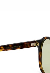 Close-up van een brillenpootje van schildpadmotief met gouden scharnier en gegraveerd modelnummer, maat en CE-markering op witte achtergrond.