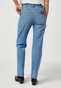 Jeans de mezclilla azul claro con corte recto, que cuentan con dos bolsillos traseros con un patrón de costura distintivo y un parche de piel de la marca en la cinturilla.