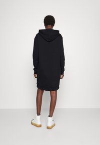 Svart sweatshirtklänning med huva, långa ärmar och rundad nederkant. Bärs med vita ankelstövlar med texturerad sula.