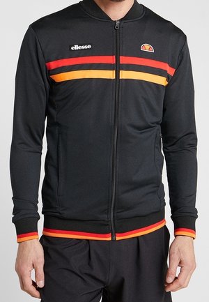 Chaqueta deportiva negra con cremallera, con rayas horizontales rojas y naranjas en el pecho y los puños, logo de ellesse en el lado izquierdo del pecho.
