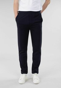 Mørkeblå, slim-fit bukser med et glat stof, elastisk talje, sidelommer og et avsmalnende ben-design. Kombinert med hvite joggesko.