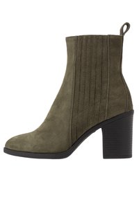 Stivale alla caviglia in suede verde oliva con tacco a blocco sovrapposto, dettagli a pannello cuciti, punta rotonda e linguetta sul retro.