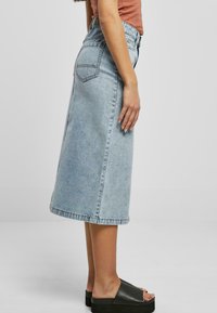 Lyseblå denim midi-skjørt med høy midje, en lett utsvingt silhuett og baklommer. Kombinert med svarte platåsandaler.