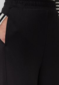 Schwarze Sporthose mit elastischem Bund, Seitentaschen und glatter Textur. Verfügt über weiße Streifenakzente an den Säumen.