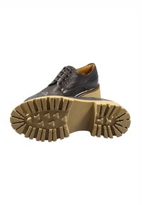 Scarpa in pelle nera con punta tonda, design a lacci e perforazioni decorative. Suola in gomma beige spessa e strutturata con motivi antiscivolo.