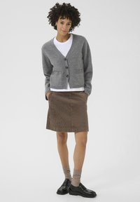 Gray knitted cardigan with v-neck and buttons, paired with a brown corduroy skirt. Model wears beige socks and black loafers.