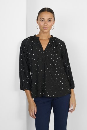 Blusa nera con pois bianchi, caratterizzata da scollatura a V, dettaglio di collo arricciato e maniche a tre quarti con polsini elasticizzati.