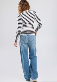 Striped ribbed long-sleeve top in white and navy, paired with light blue wide-leg jeans featuring back pockets and subtle fading on the legs.