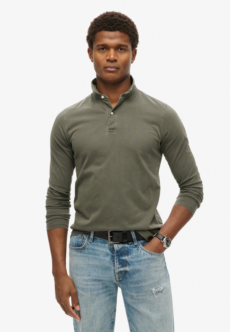 Polo de manga larga verde con una tapeta de medio botón, combinado con jeans de mezclilla azul claro. Presenta un corte relajado y una textura suave.