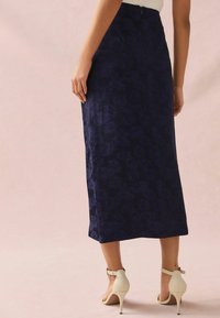 Gonna midi in tessuto navy con motivo floreale, dalla texture liscia e con chiusura a zip sul retro, abbinata a sandali bianchi con tacco alto.