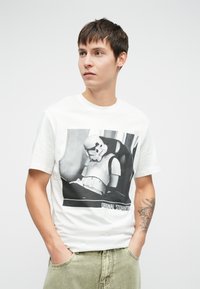 Bela bomba iz bombaža z grafiko stormtrooperja v črno-beli barvi. Majica ima okroglo ovratnik in kratke rokave.