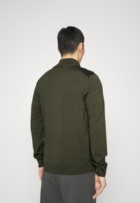 Tummanvihreä neulepusero, jossa on resorikaulus ja teksturoidut hartiaosat, pitkät hihat ja istuva vyötärönauha.