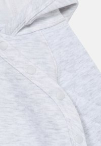 Svetlosivý mikina s kapucňou, s jemnou textúrou, diagonálnym zapínaním na cvoky a hladkým povrchom. Ideálna na bežné nosenie.