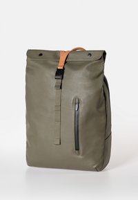 Zaino verde oliva con design a roll-top, tracolla in pelle marrone, tasca frontale con zip e superficie liscia, resistente all'acqua.