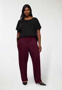 Czarna, luźna bluzka z krótkim rękawem zestawiona z wysokimi, szerokimi spodniami w kolorze burgundowym, uzupełniona czarnymi, szpiczastymi balerinkami.