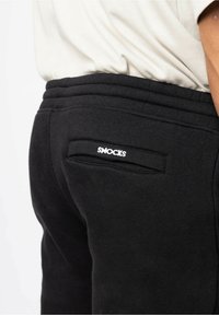Svarta sweatpants med ribbad midja och en liten bakficka som har "SNOCKS" broderat i vitt. Mjuk tyg med en slät textur.