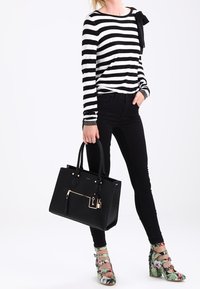 Czarna i biała w paski koszula z długim rękawem, czarne dżinsy skinny, czarna torebka z złotymi akcentami oraz buty na wysokim obcasie w kwiatowy wzór.