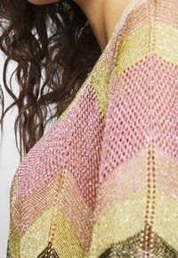 Knit garment with a chevron pattern in pink, gold, and black, featuring a breathable, metallic-textured fabric and a loose, flowy design.