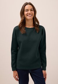 Mörkgrön sweatshirt med rund hals, långa ärmar och ribbade mudd. Slät tygkvalitet med en något avslappnad passform. Kombinerad med mörka jeans.