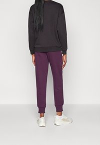 Svart sweatshirt med långa ärmar och ribbade manchetter, kombinerad med lila joggers med elastiska manchetter. Vita sneakers med texturerade detaljer.