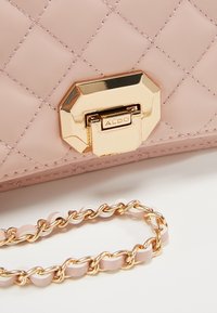 Borsa a tracolla in pelle trapuntata rosa con chiusura dorata, dotata di una catena dorata e dettagli color crema.