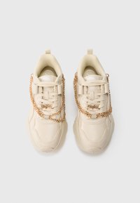 Μπεζ chunky αθλητικά παπούτσια με λεία δερμάτινη επιφάνεια, που διαθέτουν χρυσή αλυσίδα στο πλάι και υφασμένο, επενδυμένο πέλμα αστραγάλου.