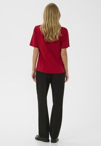 Raudona trumpomis rankovėmis marškinėlius su laisvu siluetu, derinami su juodomis plačiomis kelnėmis ir juodais batais, matomi iš nugaros.