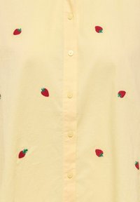 Chemise jaune clair à boutons avec de petites fraises rouges brodées dispersées sur le tissu.