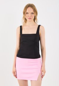Top tank nero a scollo quadrato con spalline larghe, dal design aderente. Abbinato a una mini gonna rosa con spacco laterale.