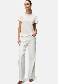 Witte, lichte T-shirt met korte mouwen en textuuraccenten, gecombineerd met wijde, crèmekleurige broeken. Neutrale sandalen maken de outfit compleet.