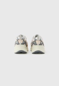 Une paire de baskets Skechers beige et grise vue de dos sur un fond clair.