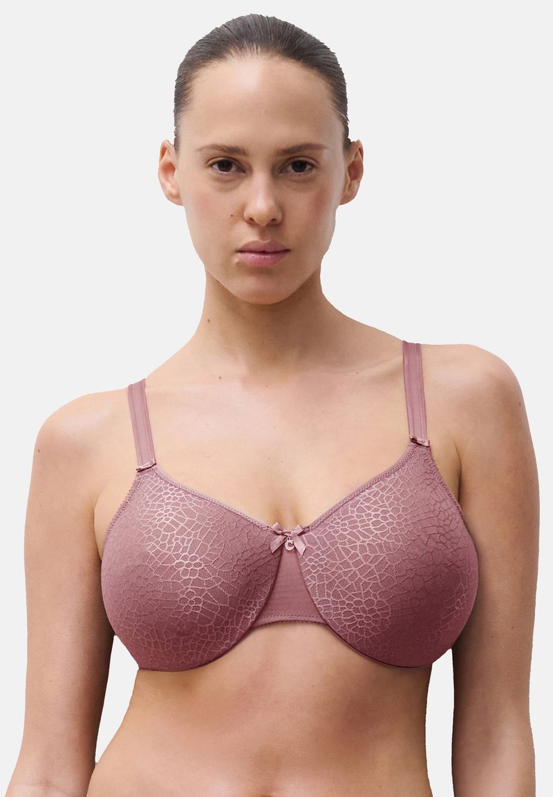 Soutien-gorge en rose doux et discret avec un motif en dentelle texturé, bonnets moulés, bretelles réglables et un petit nœud décoratif au centre.
