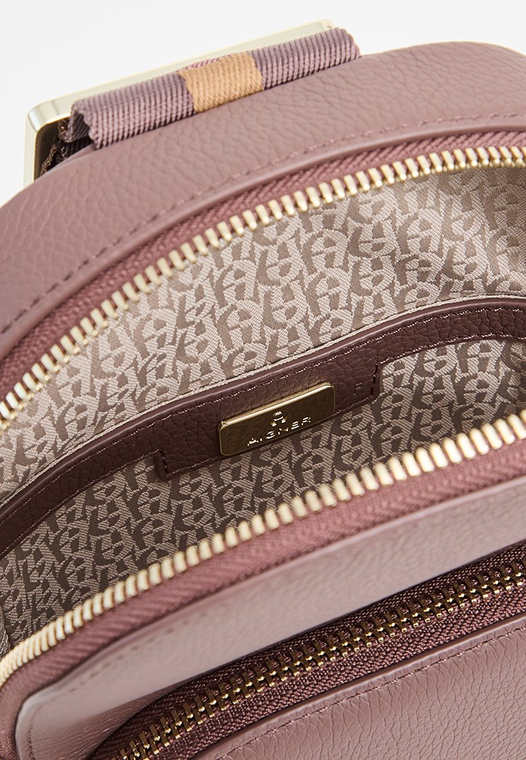 Innenansicht eines rosa Leder-Rucksacks mit geometrischem Muster, einem goldenen Hardware-Tag und einem Reißverschlussfach mit glatter Textur.