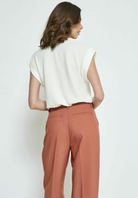 Top blanco texturizado con mangas cortas, combinado con pantalones de pierna ancha de color óxido de cintura alta. Presenta bolsillos traseros y detalles de costura mínimos.