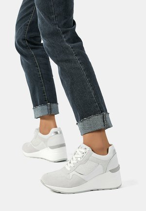 Sneakers bianche con una parte superiore testurizzata, pannelli in rete e tacco a zeppa. Accenti e lacci grigi completano il design sportivo, abbinati a denim scuro.