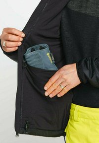 Schwarze Jacke mit einer Reißverschlusstasche, die einen grauen wasserdichten Handschuh präsentiert. Saubere Textur und taillierte Passform mit verstellbaren Hardware-Details.