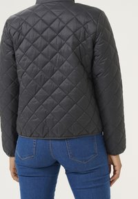 Rombebroderet sort jakke med en struktureret overflade, som har en rund krave og bund, parret med blå jeans.