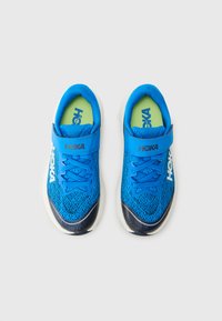 Baskets de sport bleues avec une tige en mesh respirant, dotées d'une sangle Velcro, de lacets et d'une semelle blanche contrastante. Semelles intérieures vertes visibles.