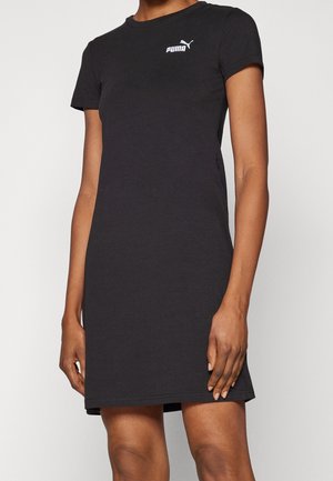 Persona con vestido Puma negro de manga corta, hasta la rodilla, con logotipo blanco en el pecho, de pie frente a un fondo liso.