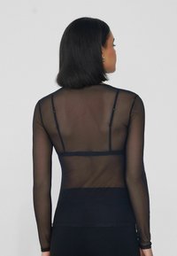 Schwarzes, durchsichtiges Langarmoberteil mit einer glatten Textur und transparentem Stoff, ausgestattet mit dünnen Trägern und einer figurnahen Silhouette am Rücken.