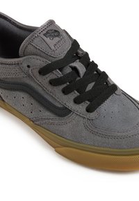 Zapatillas de skate de ante gris con detalles en negro, cordones redondos y suela de goma. Presentan perforaciones y un parche con el logo en la lengua.