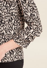 Korte mouwtop in crème met een gedurfde zwarte dierenprint. Voorzien van een ritsdetail aan de zijkant en een textuurstof.