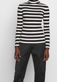 Maglione a maniche lunghe a collo alto a righe bianche e nere, con una silhouette aderente e una morbida texture del tessuto. Abbinato a pantaloni cargo neri.