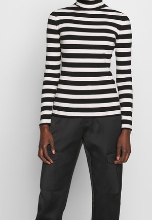 Maglione a maniche lunghe a collo alto a righe bianche e nere, con una silhouette aderente e una morbida texture del tessuto. Abbinato a pantaloni cargo neri.